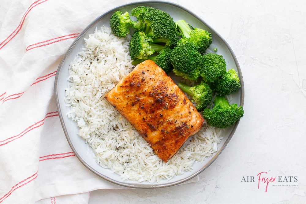 a fillet of cooked salmon on a round plate with rice and broccoli