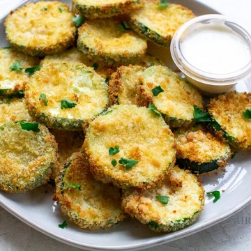 a plate of fried zucchini coins garnished with green onions and served with a white sauce
