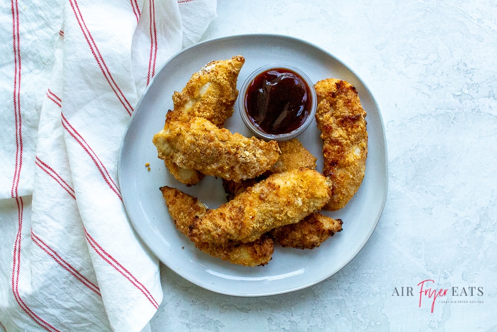 air fried chicken tenders on a round white plate with a small cup of barbecue sauce
