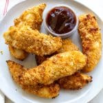 air fried chicken tenders on a round white plate with a small cup of barbecue sauce