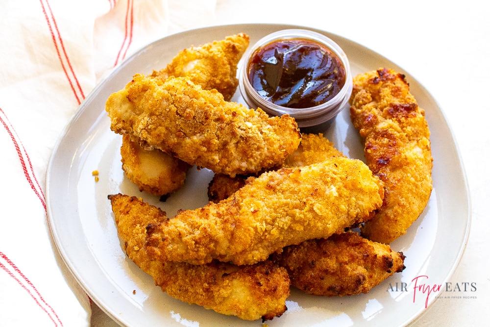 air fried chicken tenders on a round white plate with a small cup of barbecue sauce