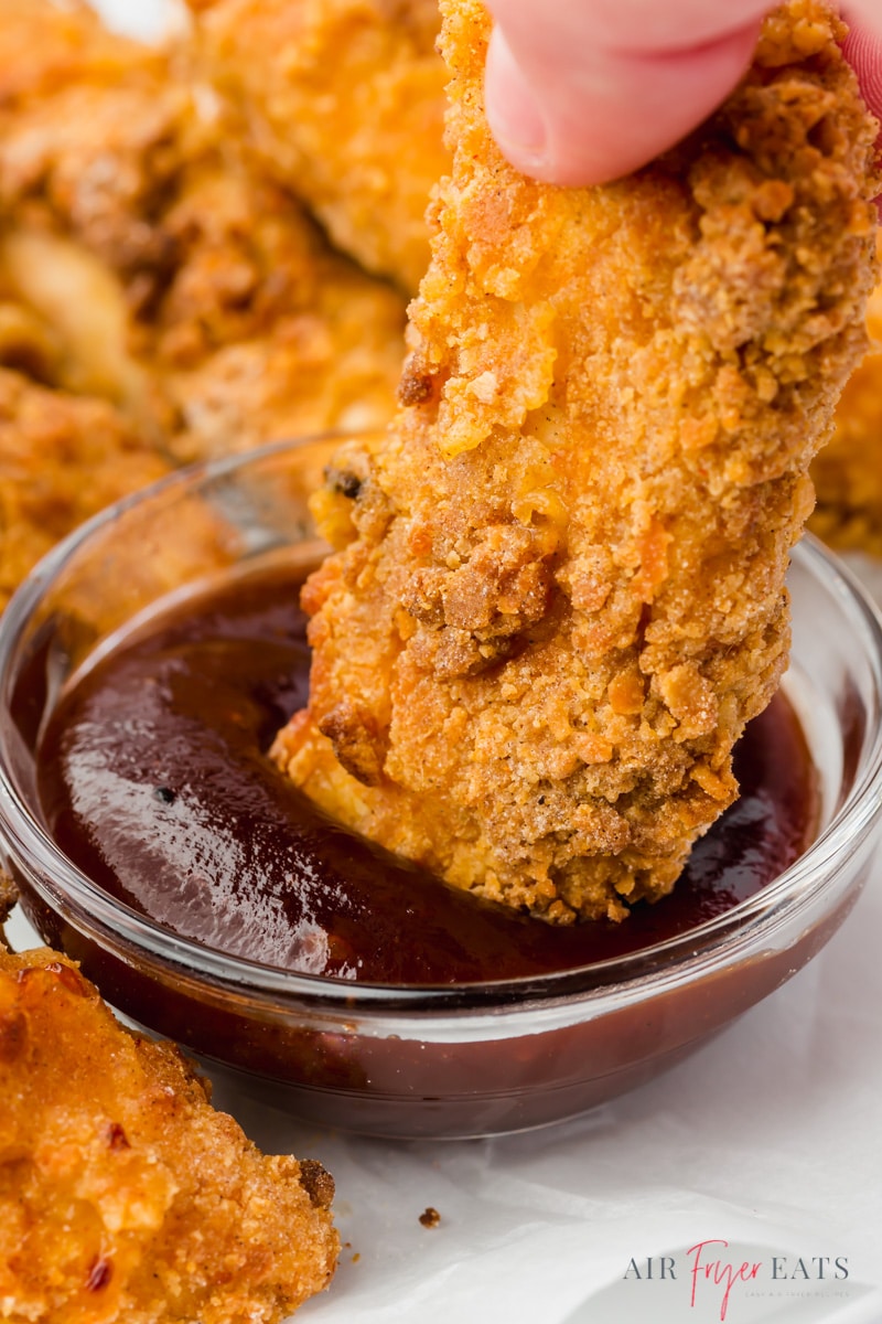 a crispy air fryer chicken tender being dipped into bbq sauce, closeup shot