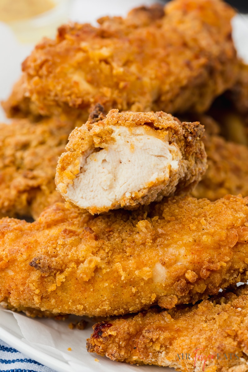 A pile of air fryer chicken tenders with one cut in half to show the meat in the middle.
