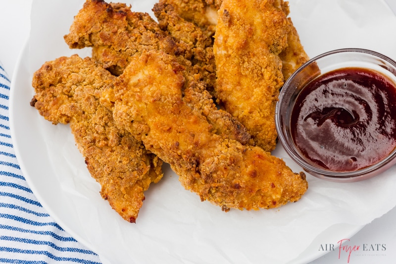 a white plate filled with air fryer chicken tenders and a side of bbq sauce