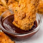 a crispy chicken tender being dipped into bbq sauce