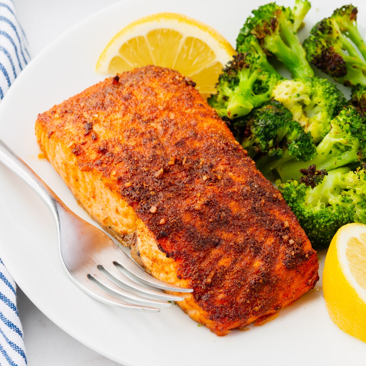 closeup of a pice of air fryer salmon on a plate with broccoli and lemon wedges