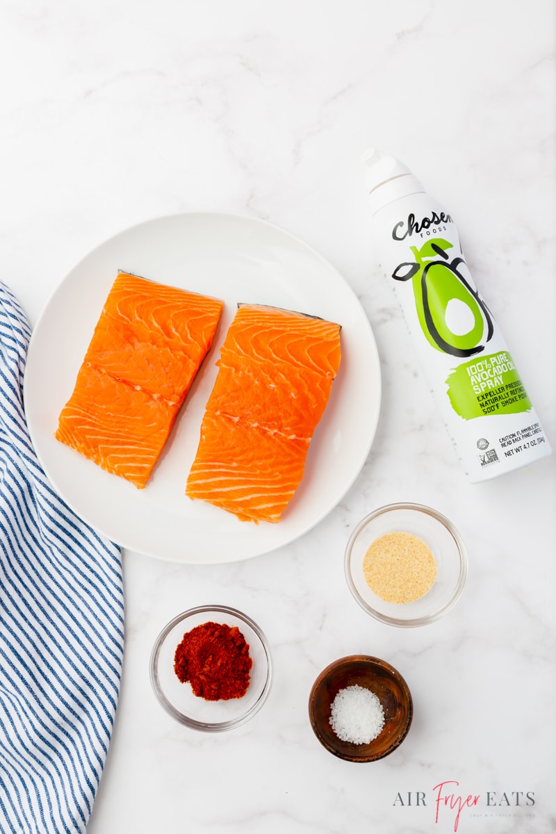 The ingredients for making salmon air fryer, including two salmon pieces, oil spray, and seasonings.