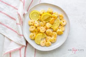 shrimp and slices of lemon on a white plate with a striped red and white towel