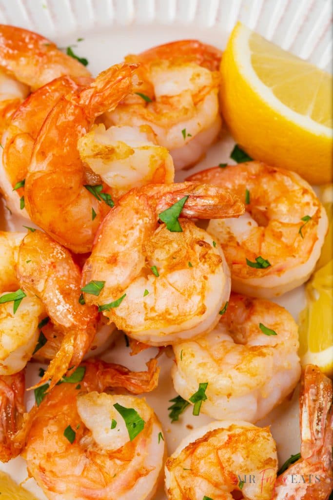 a plate of seasoned air fryer shrimp with lemon wedges on the side