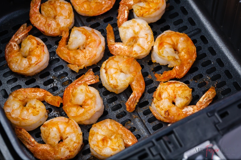 Cooked shrimp in a single layer inside of a square air fryer basket