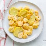 pink cooked shrimp and lemon slices on a round white plate