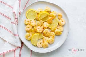 pink cooked shrimp and lemon slices on a round white plate