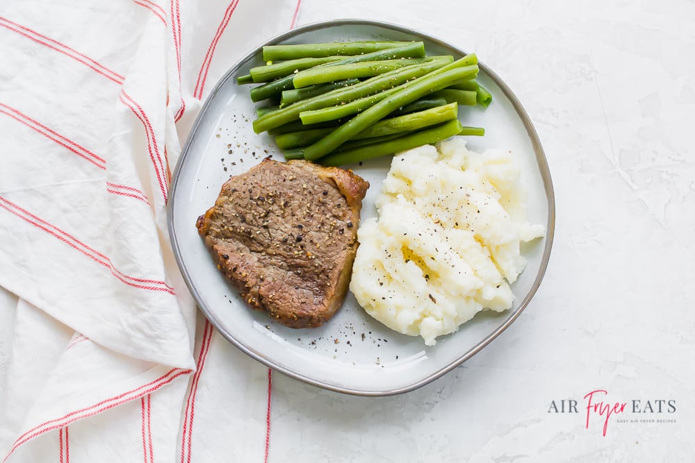 a white plate of steak, green beans, and mashed potatoes