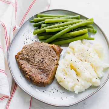 steak with mashed potatoes and green beans on a plate over a red and white striped towel