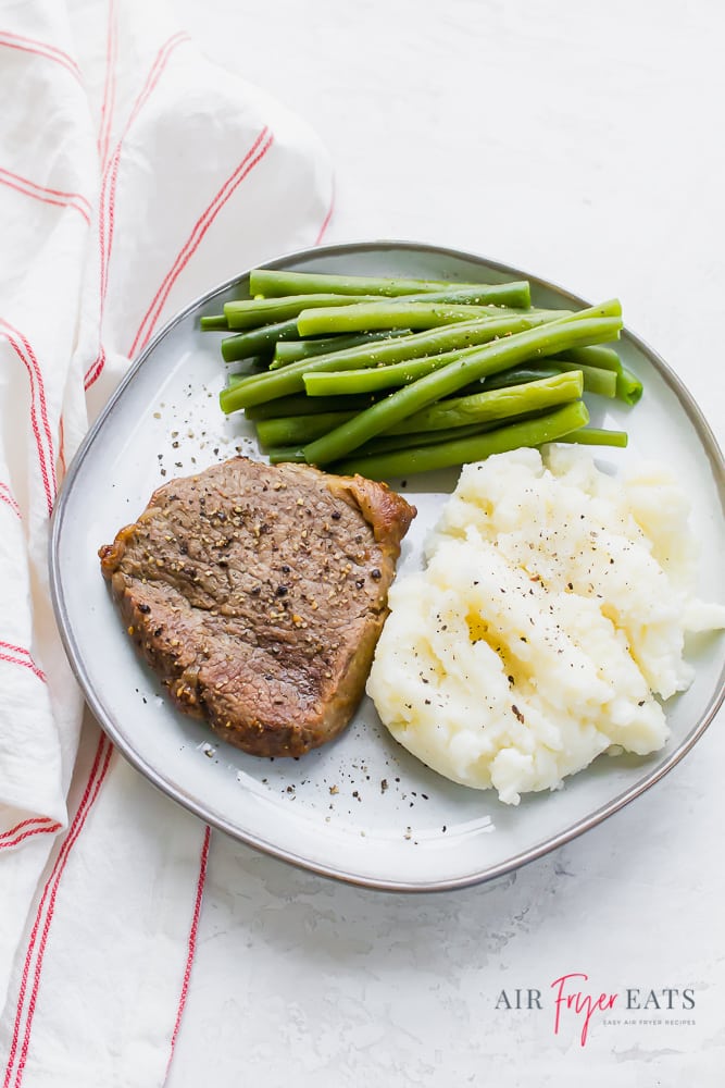 steak with mashed potatoes and green beans on a plate over a red and white striped towel