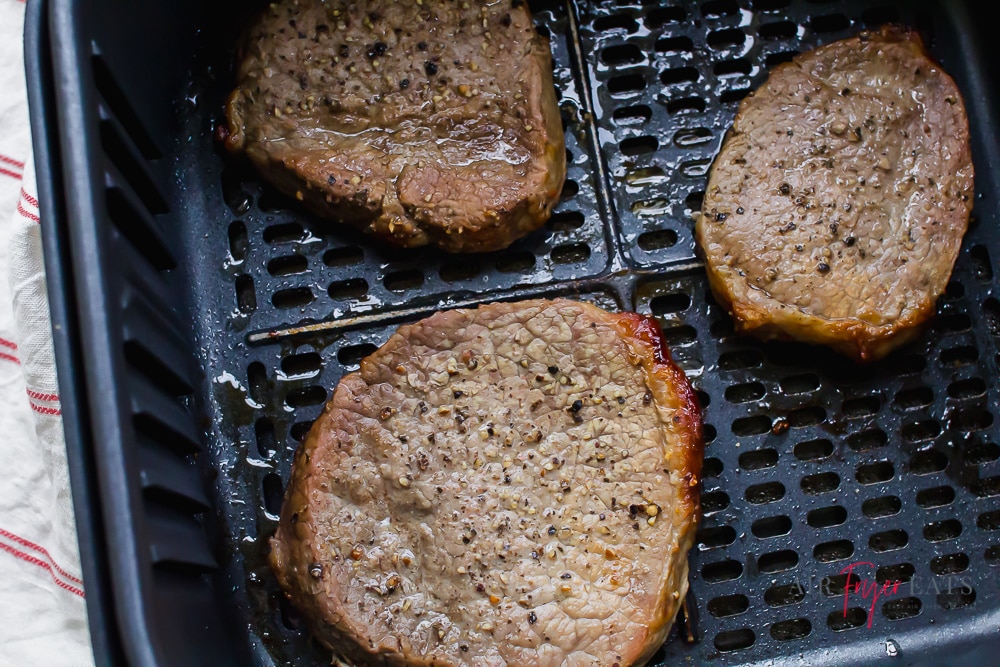 three filets of steak in a black air fryer basket