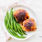 two chicken thighs with a side of green beans on a white plate