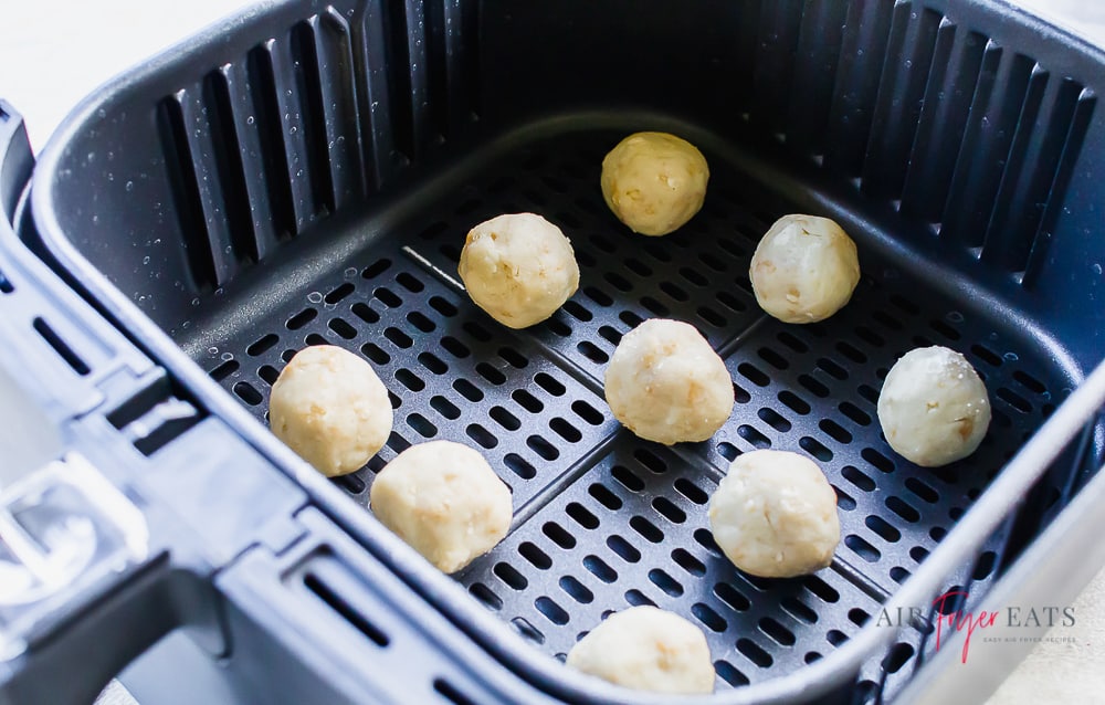 uncooked donut holes spaced out in a black air fryer basket