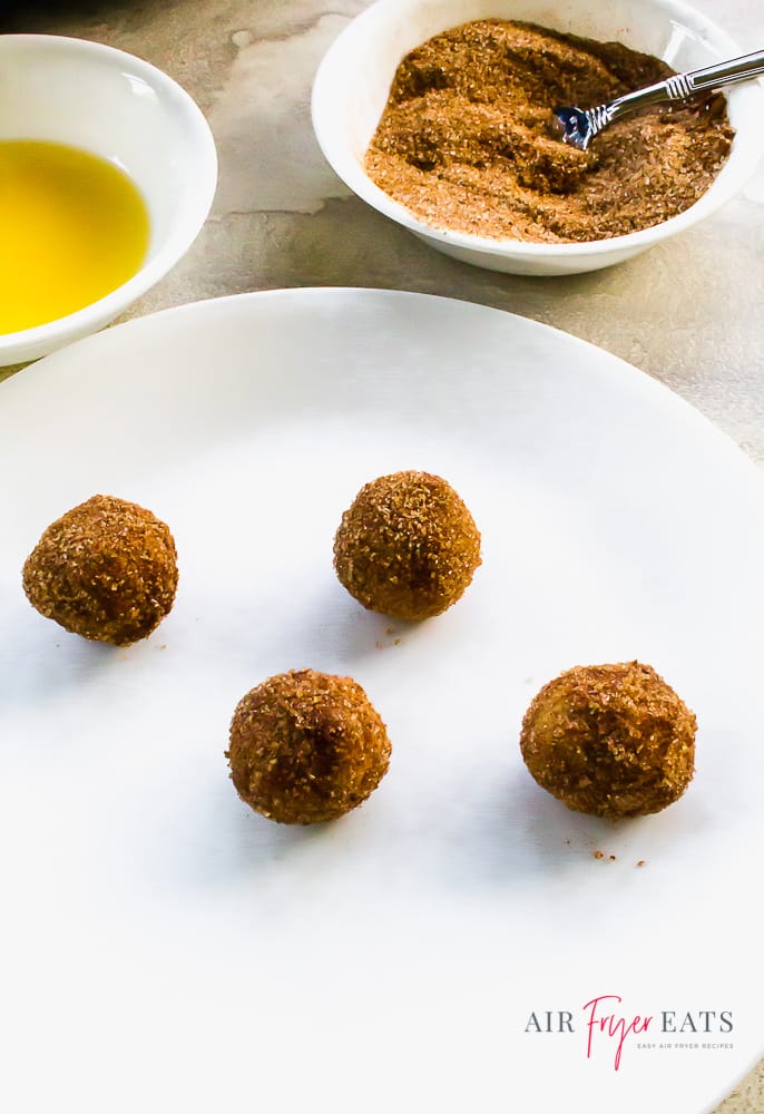 four donut holes on a white plate next to bowls of melted vegan butter and cinnamon sugar