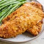 breaded fish with green beans on a white plate