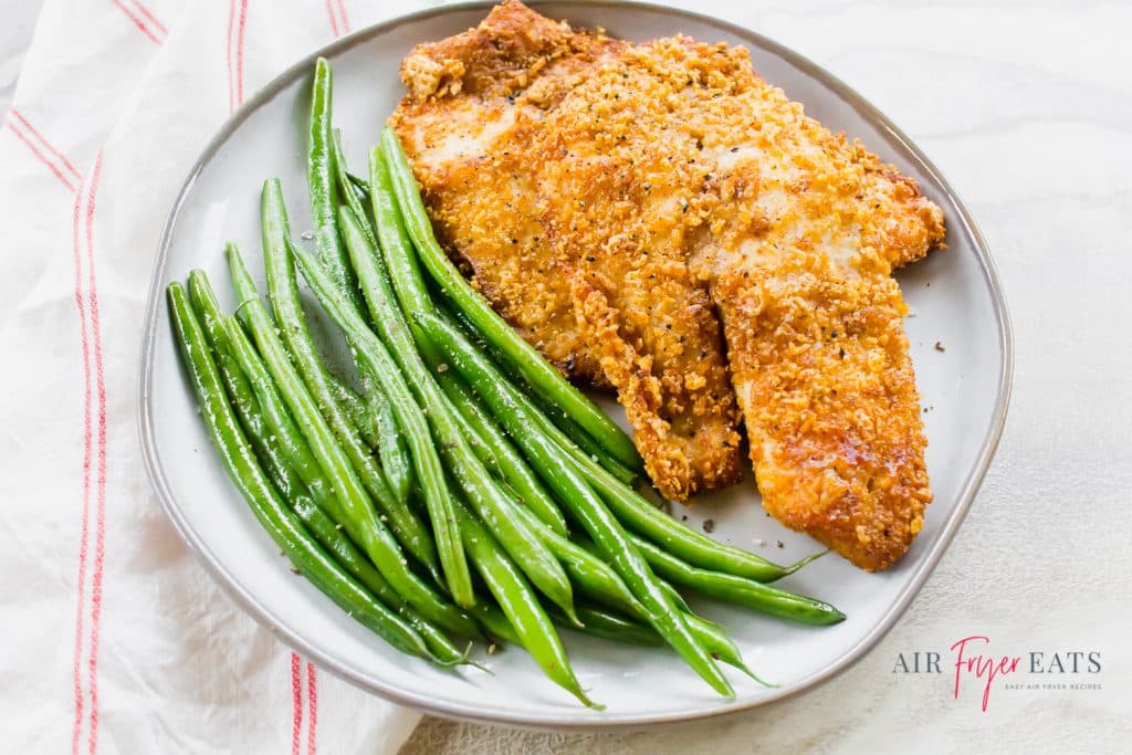 breaded fish with green beans on a white plate