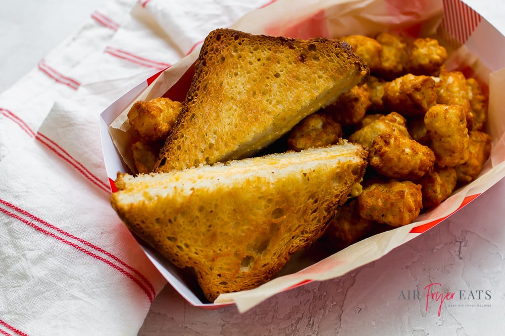 a diagonally sliced grilled cheese sandwich in a paper basket with tater tots