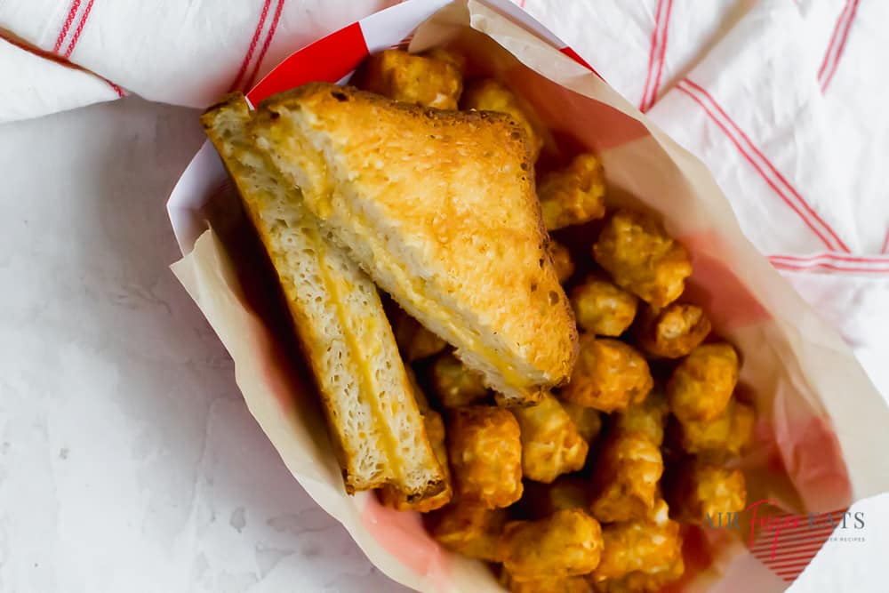 a grilled cheese sandwich in a paper basket with tater tots