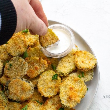 a hand dipping a fried pickle slice into a cup of ranch dressing
