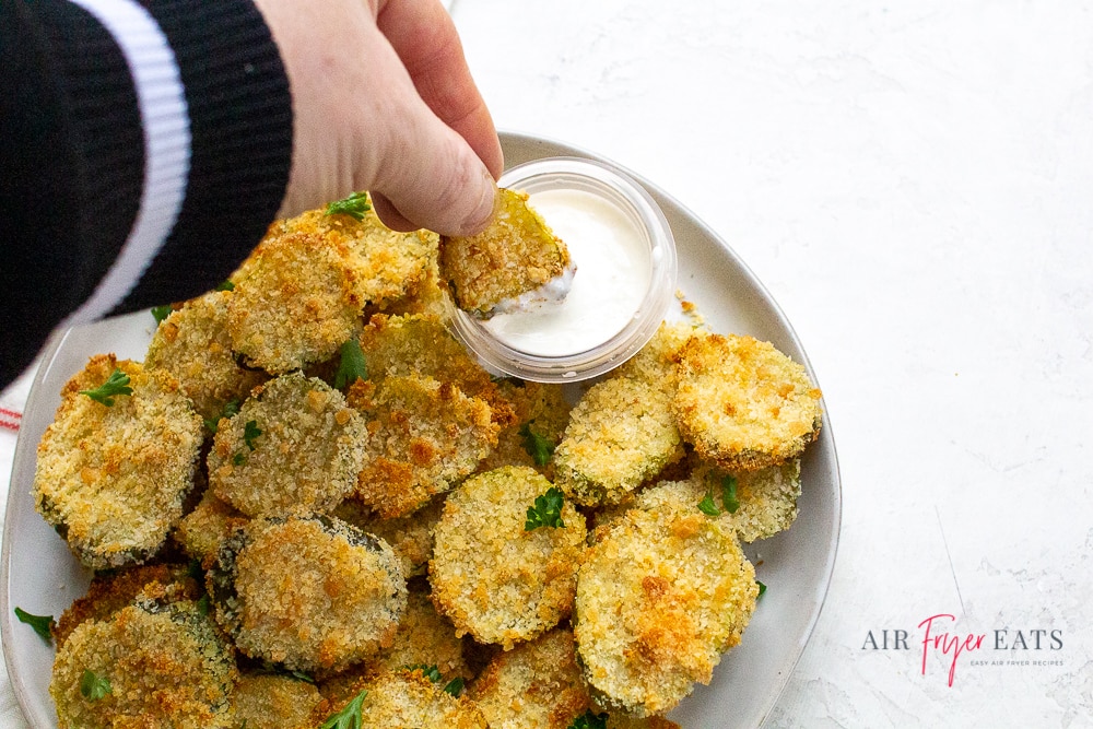 a hand dipping a fried pickle slice into a cup of ranch dressing