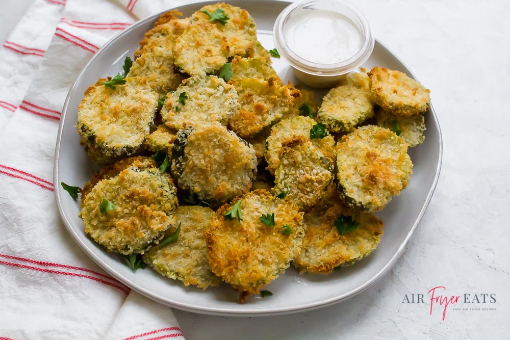 fried round slices of pickles garnished with green herbs on a white plate