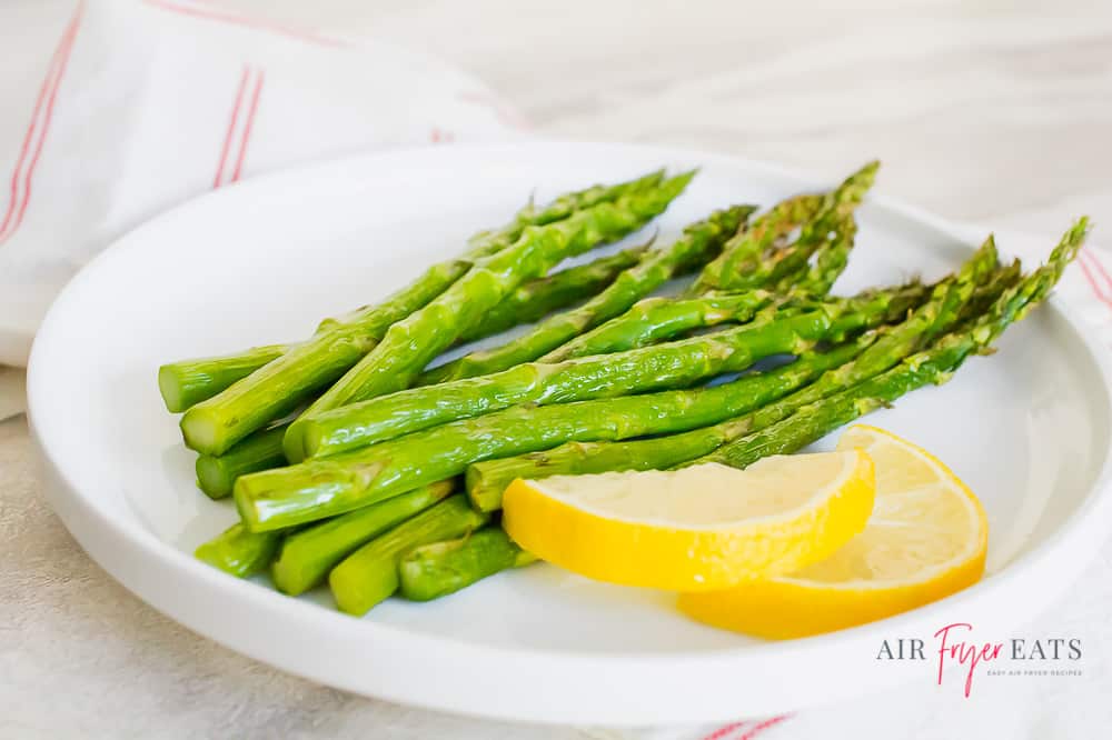 Cooked asparagus and lemon wedges on a white plate