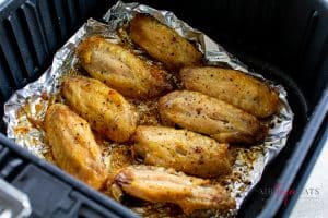 golden brown chicken wing pieces in air fryer basket sitting on top of foil