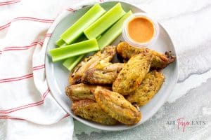 a plate of chicken wing pieces and a cup of orange dressing topped