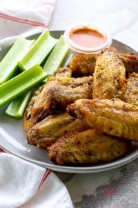 a plate of chicken wing pieces and a cup of white dressing topped with green herbs