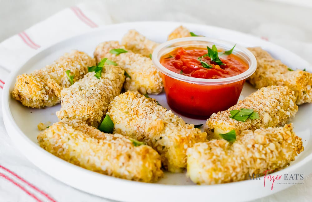 mozzarella sticks and a cup of marinara sauce on a white plate