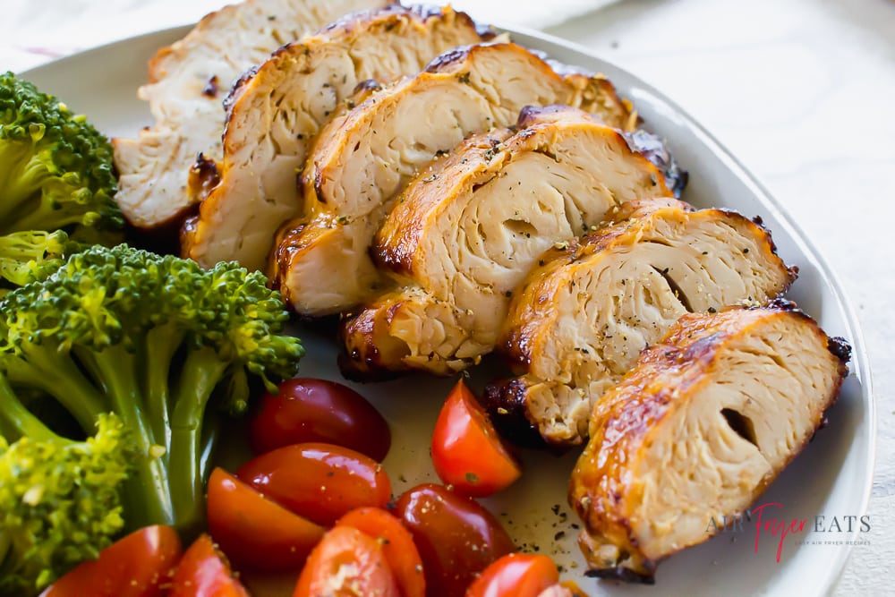 sliced seasoned turkey breast on a white plate with cherry tomatoes and steamed broccoli