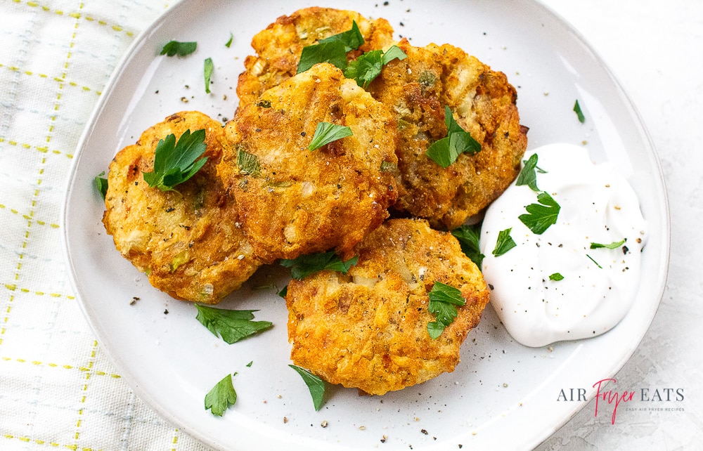 mashed potato pancakes garnished with parsley on a white plate with sour cream