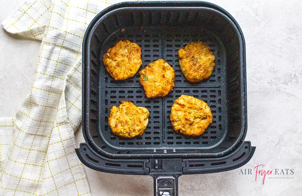 mashed potato pancakes in air fryer basket next to a white kitchen towel