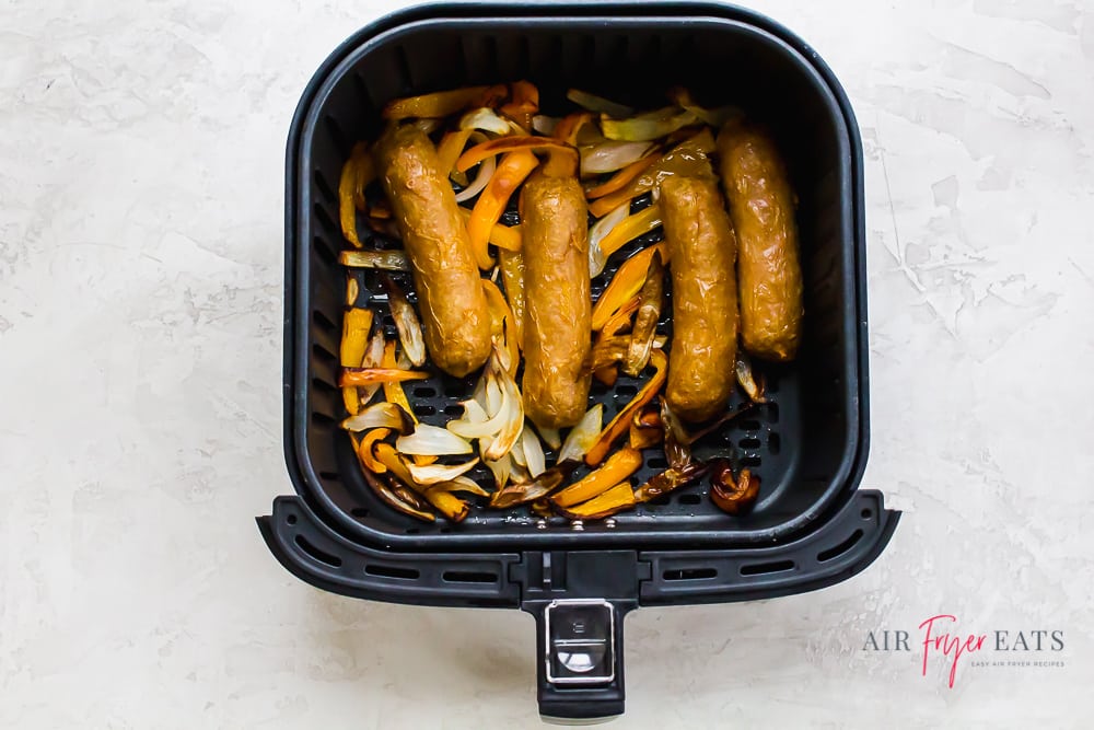 cooked brats, bell pepper, and onions in an air fryer basket