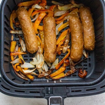 Cooked brats, bell peppers, and onions in an air fryer basket