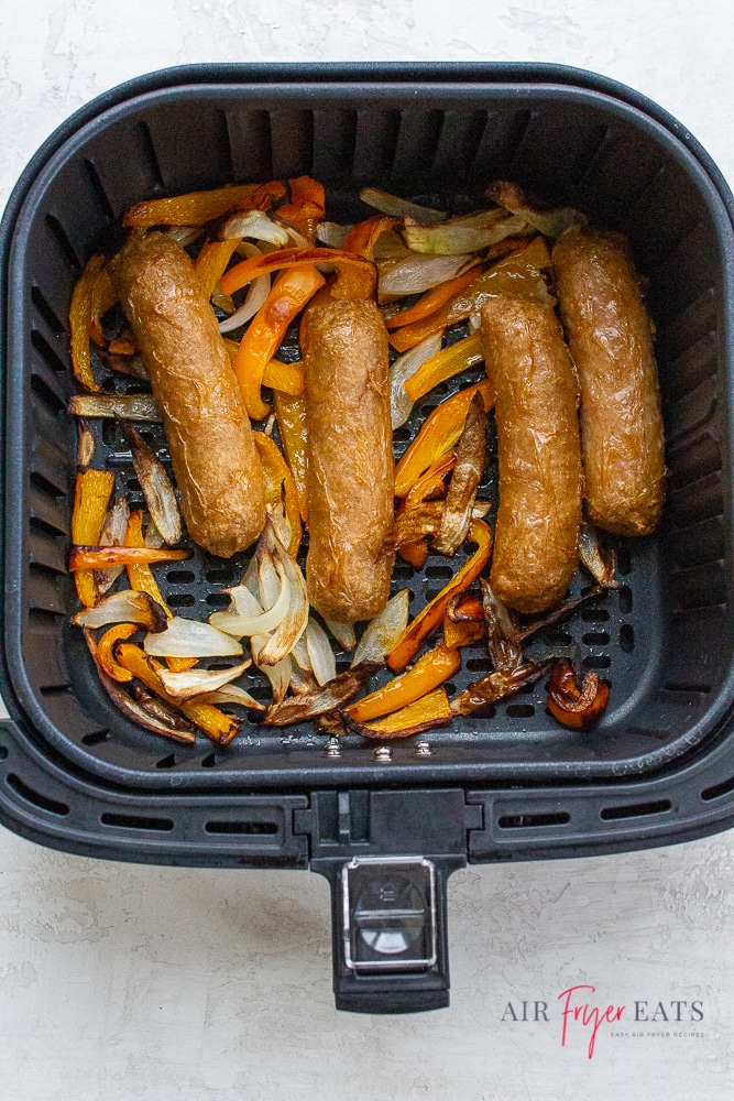 Cooked brats, bell peppers, and onions in an air fryer basket