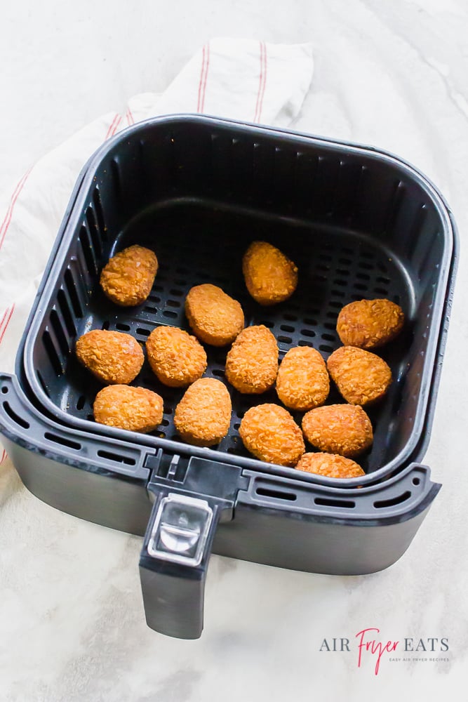 Vertical picture of black air fryer basket with cooked chicken nuggets on a white background.