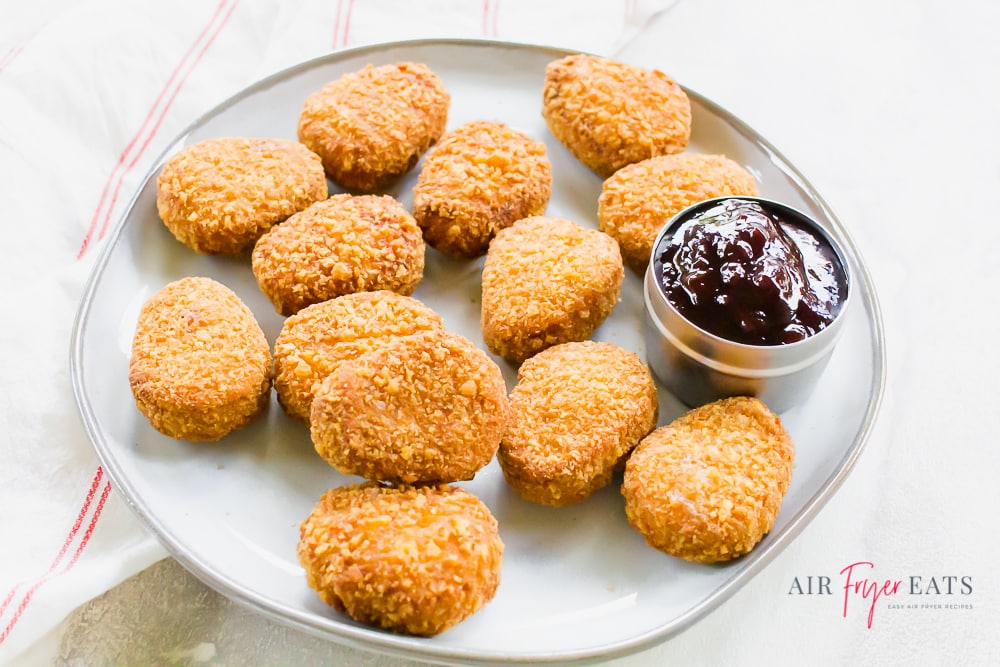 Cooked nuggets on a white plate on a white back ground. Small cup of marroon dipping sauce.