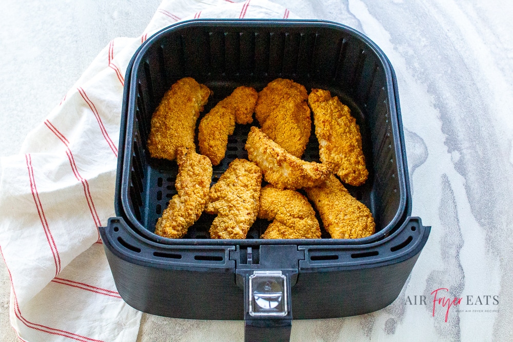 Cooked Tyson air fried chicken in a black air fryer basket on a white background. White napkin with a thin red strip to the left and top of the air fryer basket.