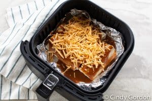 uncooked vegetarian enchiladas topped with sauce and cheese in an air fryer basket