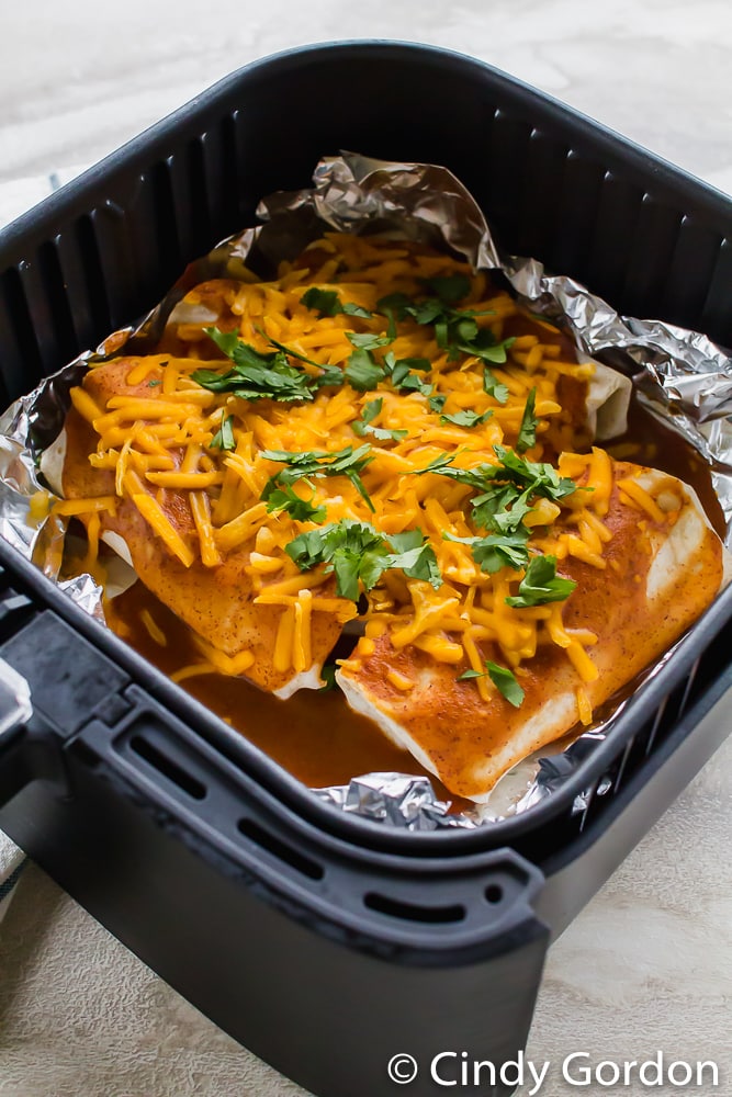 vegetarian enchiladas topped with shredded cheese and cilantro in an air fryer basket coated with aluminum foil