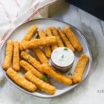 golden brown cooked fish sticks on white plate with white dipping sauce
