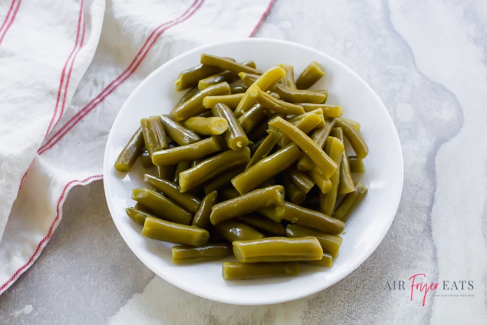 green beans in a white bowl on a white background. White and red napkin to the left.