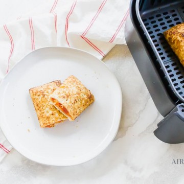 hot pocket cooked and sliced in half then stacked on a white plate. Black air fryer basket to the right with cooked hot pocket on the inside.