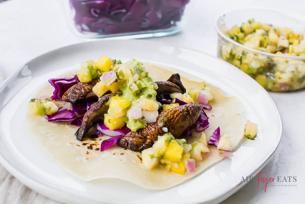 sliced portobello mushrooms with pineapple salsa, guacamole, and red cabbage on a tortilla